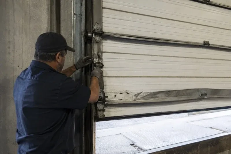 Person holding tools at the side hinge of a partly raised industrial sectional door — Commercial Sectional Door Repair, Brampton